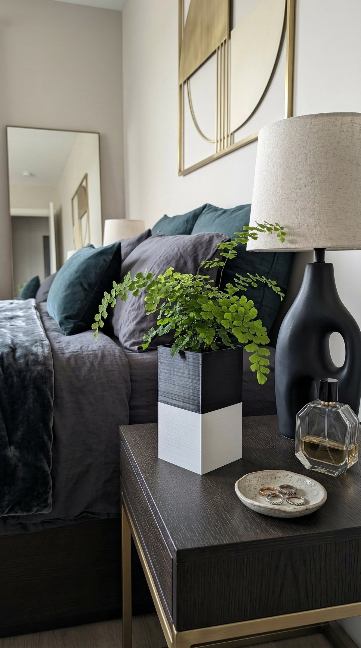 Cache-pot Le Cube bicolore noir et blanc Éclance pour pot de 6cm, contenant une fougère délicate, posé sur une table de chevet en bois sombre. En arrière-plan, une chambre élégante avec des coussins en velours bleu canard et gris.