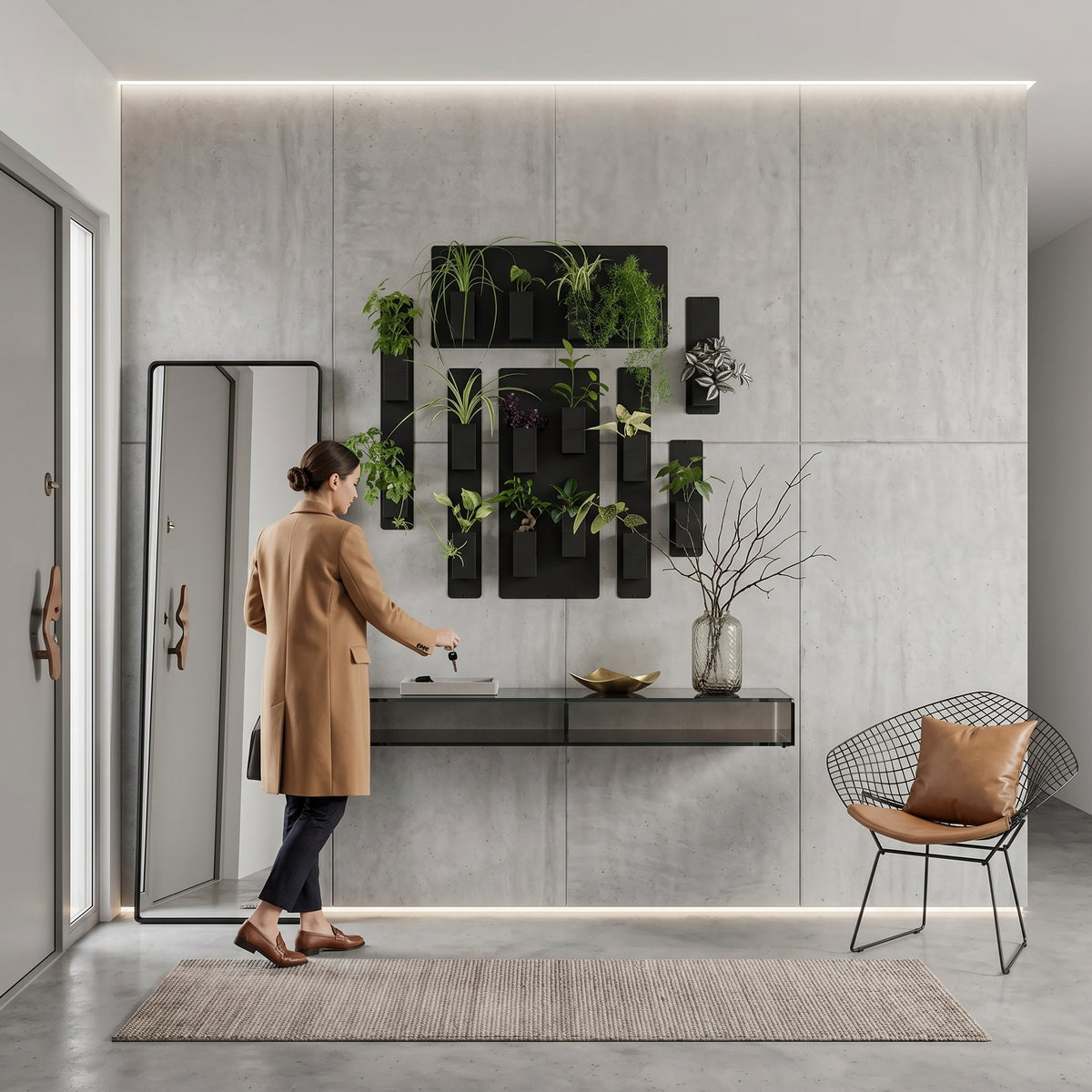 Aménagement d'une entrée moderne et chic par Éclance décoration intérieur végétal. Sur un grand mur en panneaux de béton brut rétroéclairé par des lignes de LED, une composition murale végétale est fixée sur des plaques magnétiques noires. Elle comprend plusieurs cache-pots Le cube tout noir, adaptés pour des pots de 6cm, remplis de plantes vertes d'intérieur. Une femme en manteau camel dépose ses clés sur une console suspendue noire. Un grand miroir vertical, un tapis tressé et une fauteuil design .
