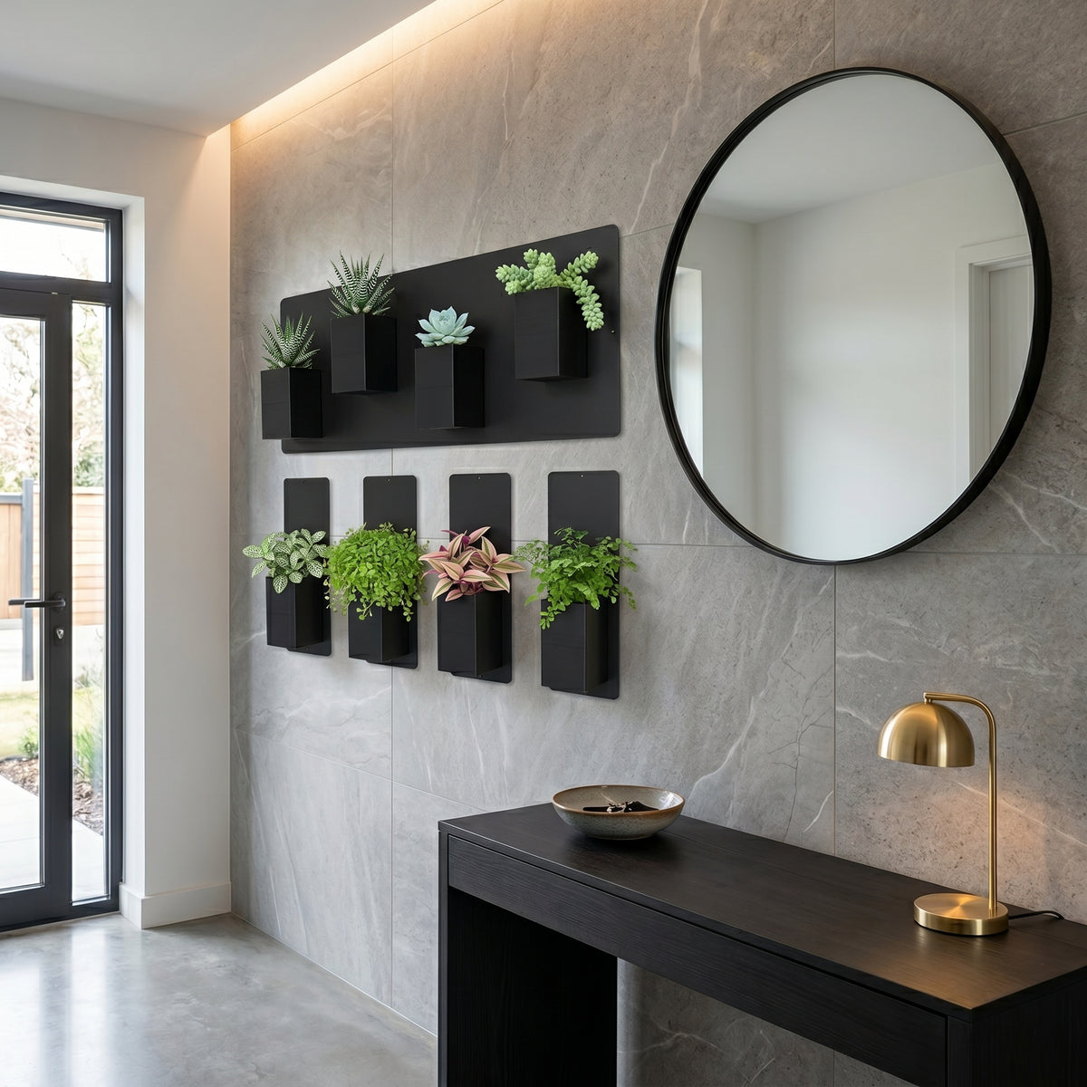 Aménagement biophilique et luxueux d'un hall d'entrée contemporain par Éclance décoration intérieur végétal. Sur un grand mur revêtu de dalles effet marbre gris veiné de blanc, éclairé par un bandeau LED indirect au plafond, un mur végétal modulaire associe une plaque magnétique noire horizontale et quatre plaques verticales fines. Plusieurs cache-pots Le cube tout noir (conçus pour des pots de 6cm) y sont aimantés, accueillant des succulentes et des plantes vertes.
