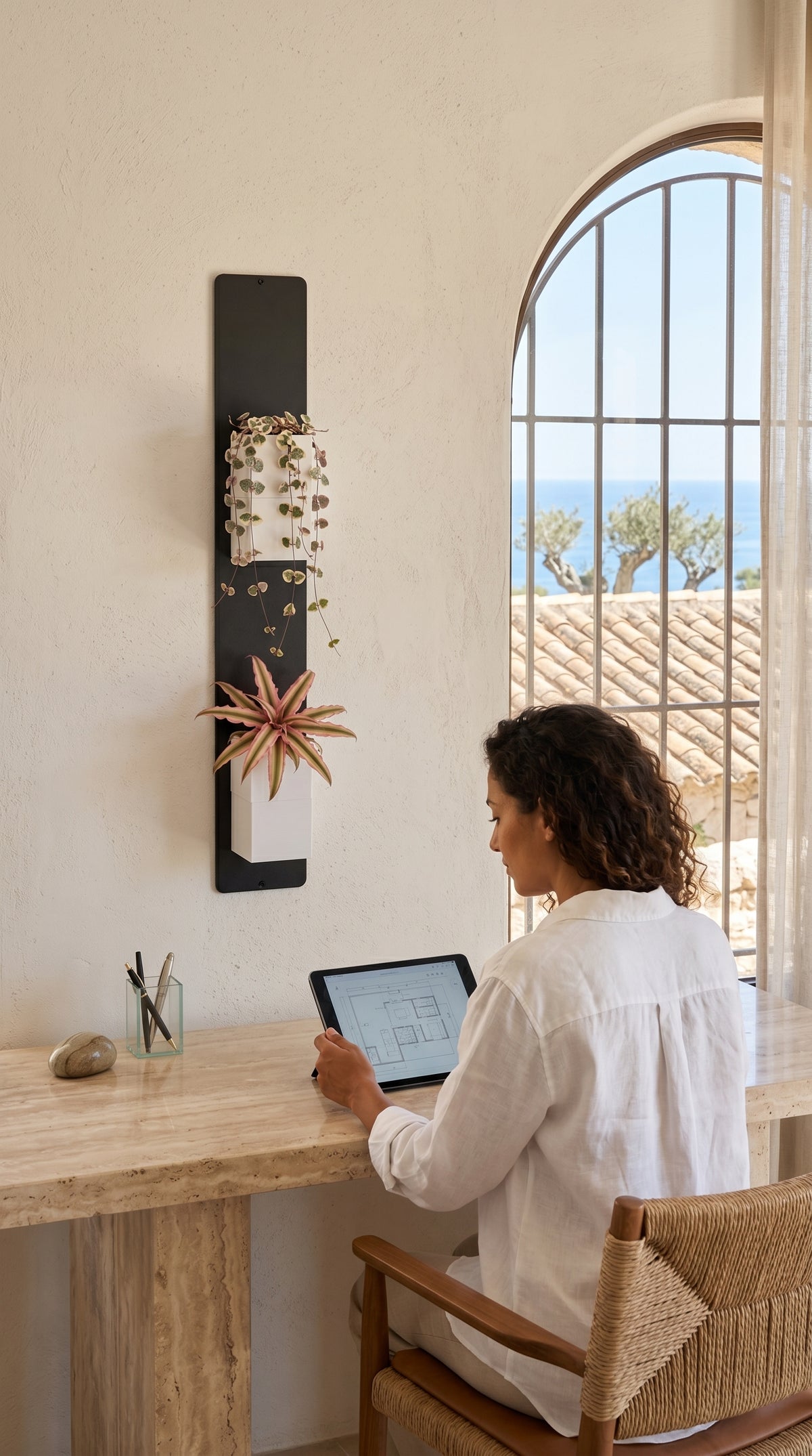 Support mural noir Éclance décoration intérieur végétal accueillant deux cache-pots blancs Le cube (adaptés pour un pot de 6cm), fixé à côté d’un bureau en travertin et d’une fenêtre en arche avec vue sur la mer.