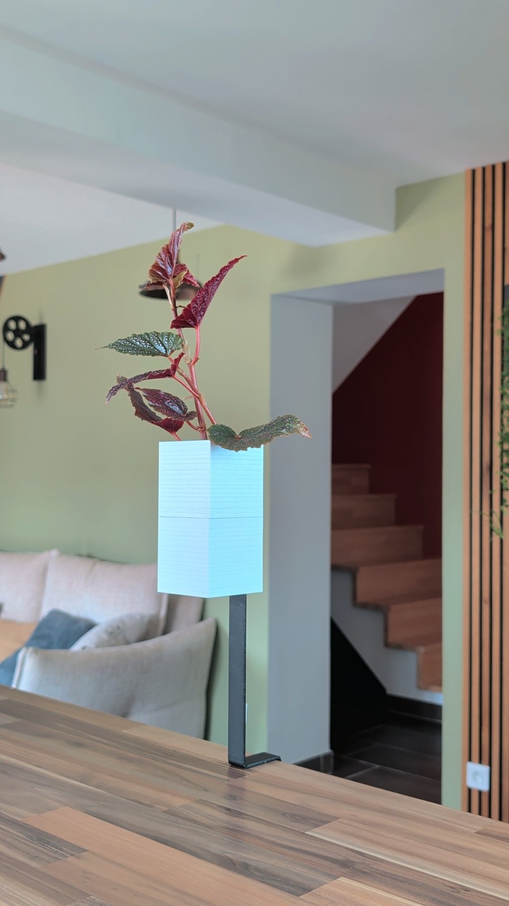 L'Îlot Végétal Éclance simple blanc : support de plante blanc fixé au rebord d'une table dans un intérieur moderne chaleureux.