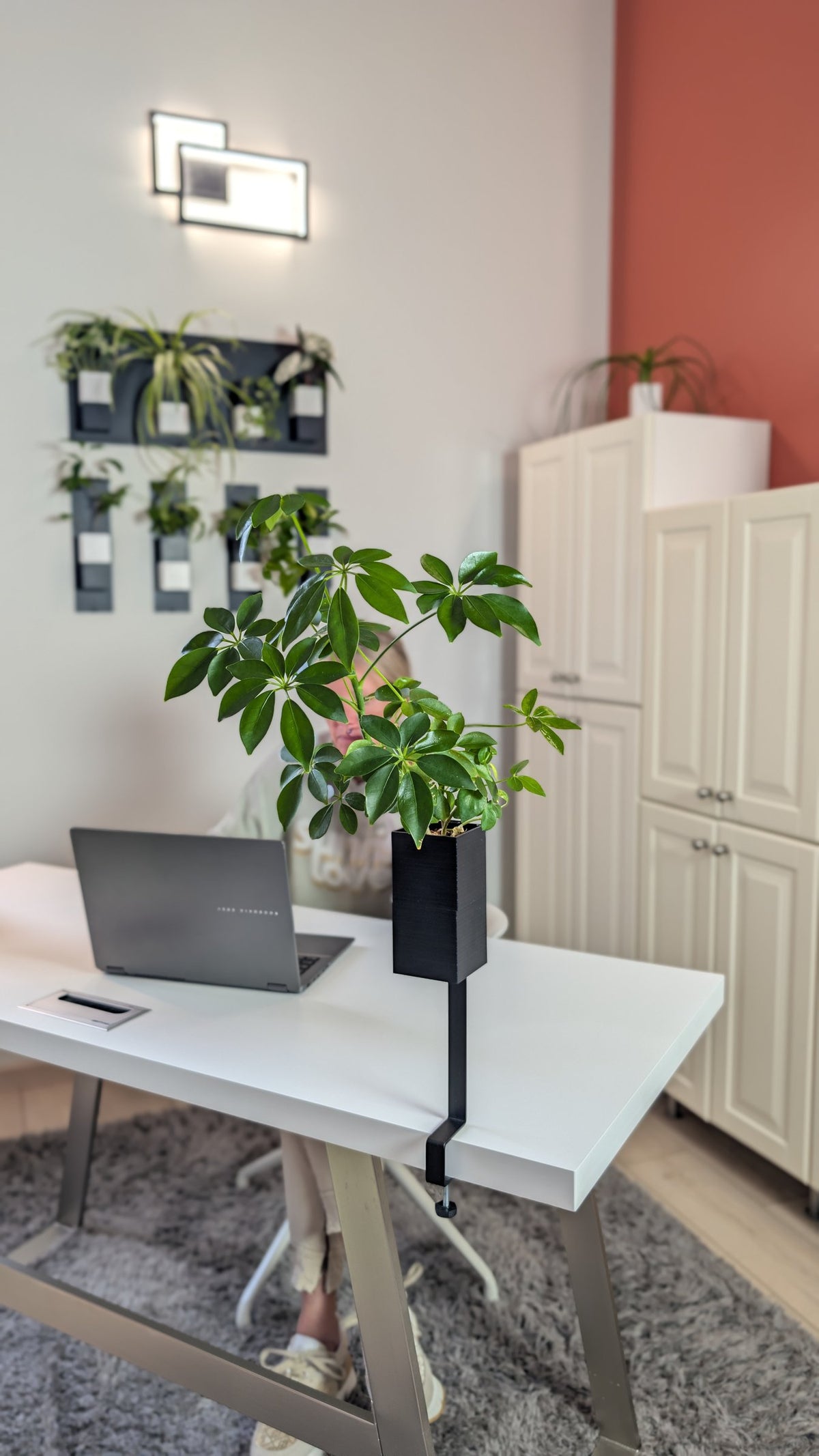 L'Îlot Végétal Éclance simple noir : un pot végétal noir fixé sur le bord d'un bureau blanc dans un espace de travail lumineux.
