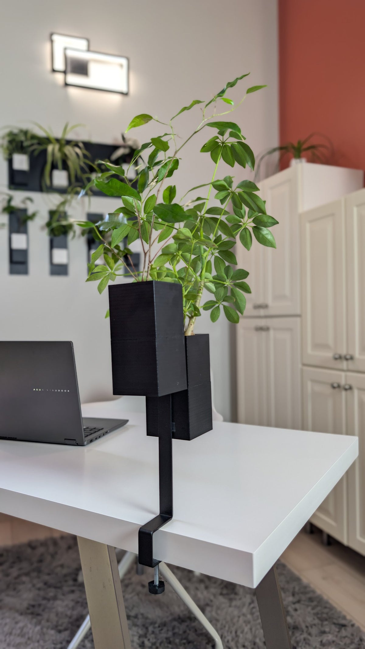 L'Îlot Végétal Éclance double noir : support pour plante noire fixé par pince sur le rebord d'un bureau blanc moderne.