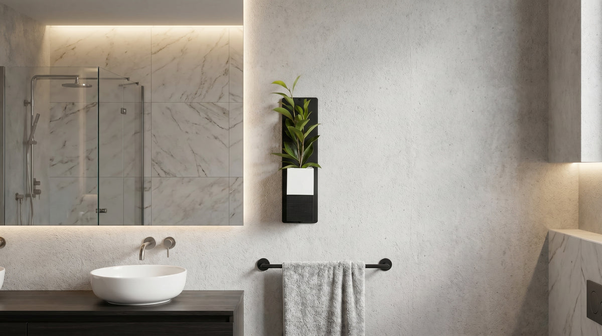 Décoration d'intérieur végétale Éclance installée dans une salle de bain moderne au design épuré. Un mini mur végétal composé d'une plaque en acier noir et d'un cache-pot Le Cube bicolore blanc et noir, adapté pour un pot de 6cm, est fixé au mur à côté d'un grand miroir éclairé et au-dessus d'un porte-serviette noir.