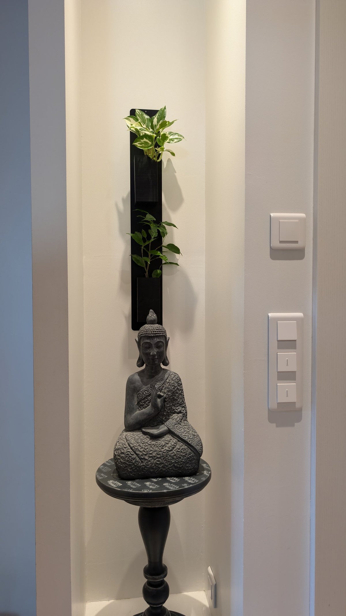 Mini mur végétal Éclance M2 noir : support mural végétal noir Mini Mur Éclance fixé dans une niche au-dessus d'une statue de Bouddha.
